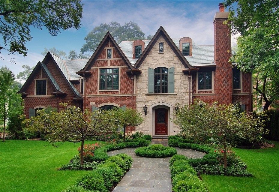 Brick and stone Maple Residence with steep gables, a garden path and mature planting.