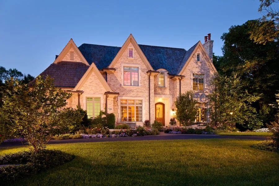 Gabled stone SGE residence photographed at dusk across a broad lawn.