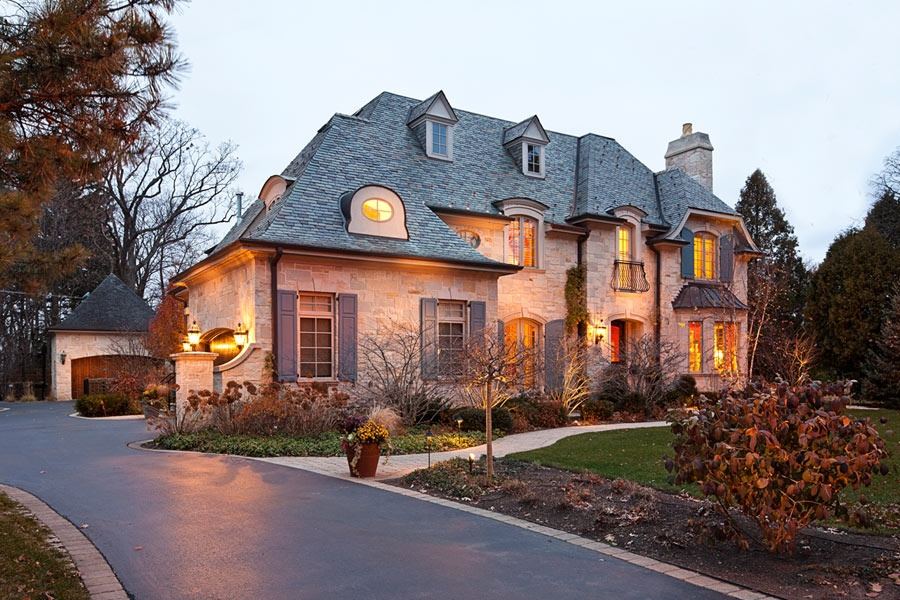Stone residence photographed at dusk with a curved drive and warm interior illumination.