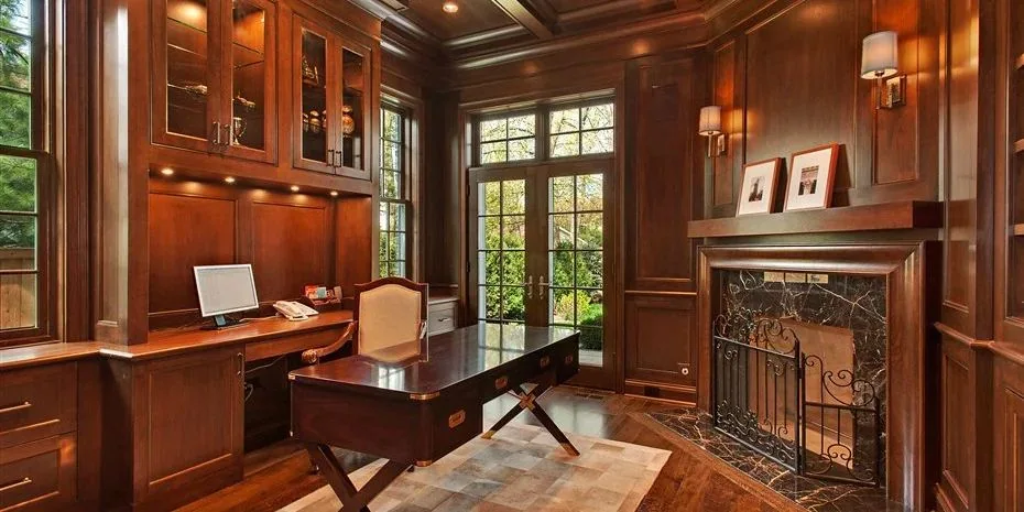 Warm wood-paneled private study with built-in cabinetry, desk and fireplace.