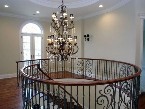 Upper-floor view across a curved stairwell with ornamental iron balusters and a tall arched window.