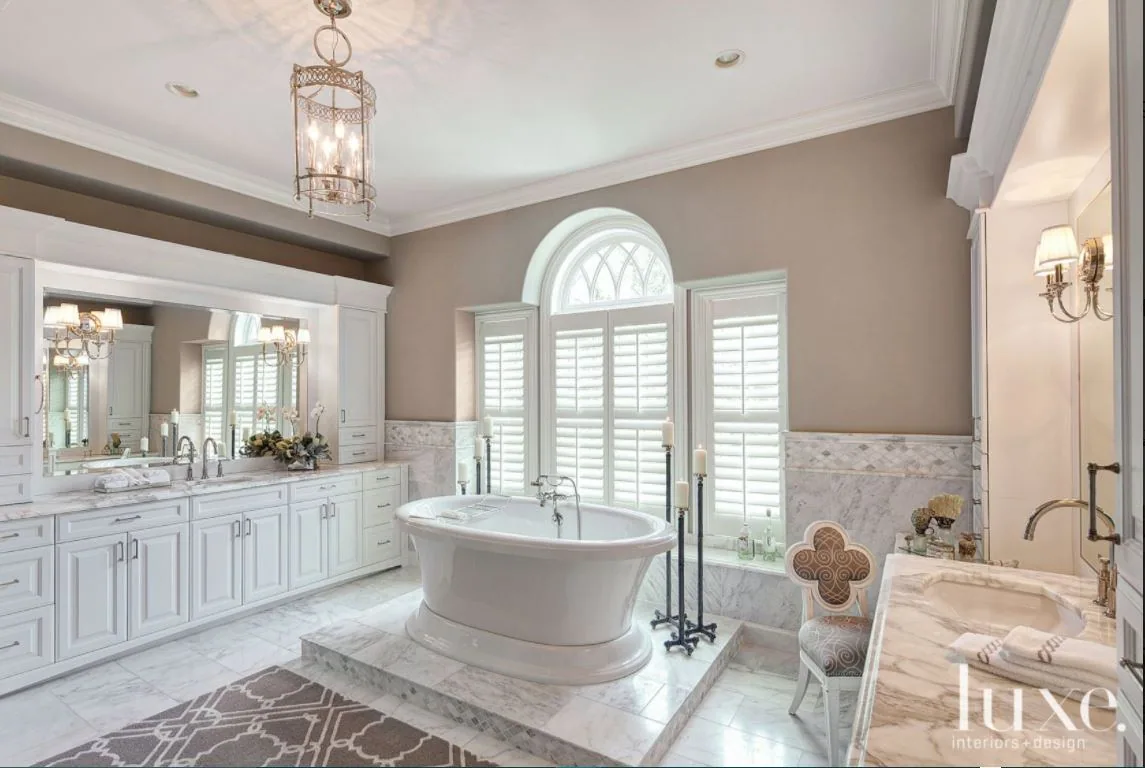 Light-filled bath with freestanding tub, arched window and pale cabinetry.