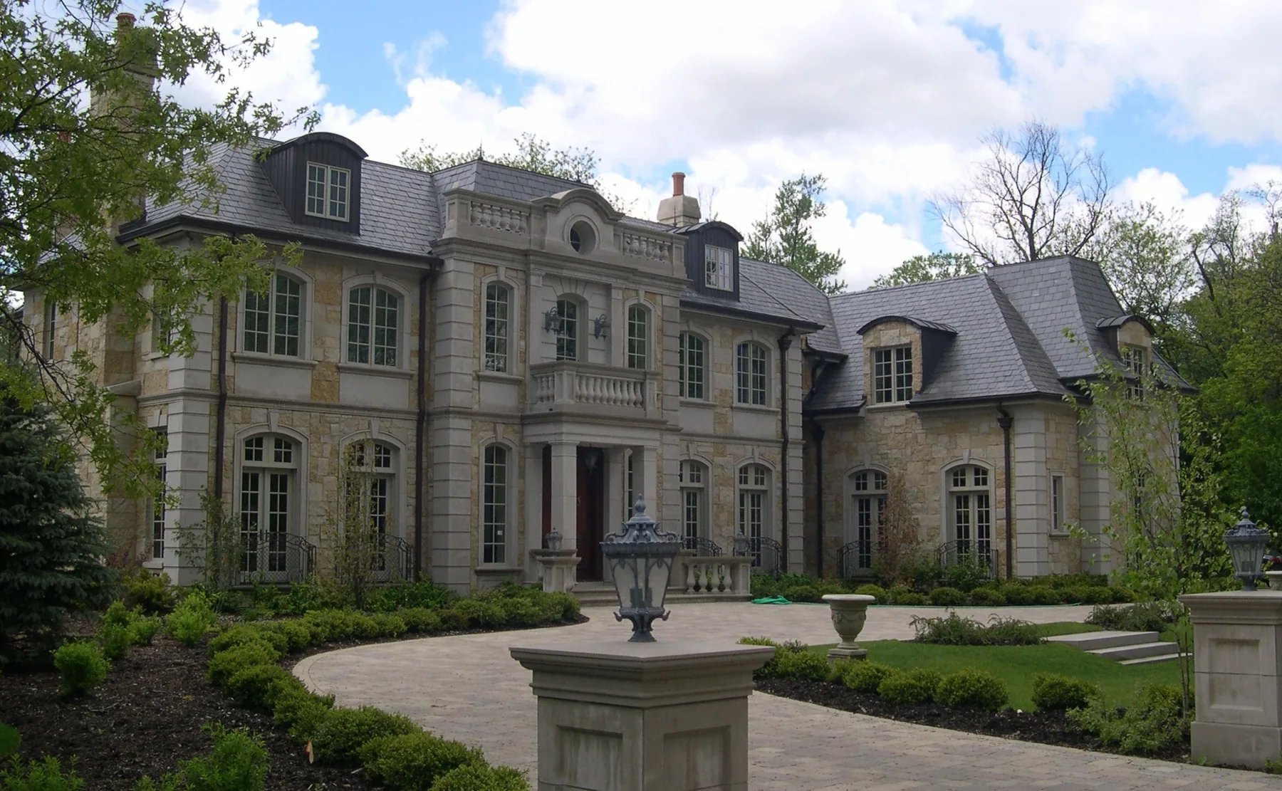 Formal stone residence with slate roof, circular drive and mature landscaping.
